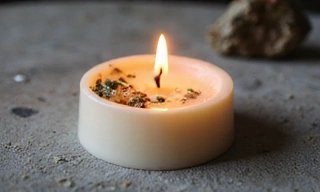 Świeca sojowa z zatopionymi ziołami, na kamiennym tle.